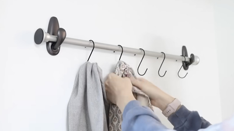 Woman's hands hanging scarves on s-hooks attached to homemade rail rack.