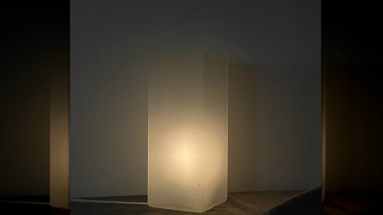 A lit GRÖNÖ lamp, sitting on a shelf, in a dark space