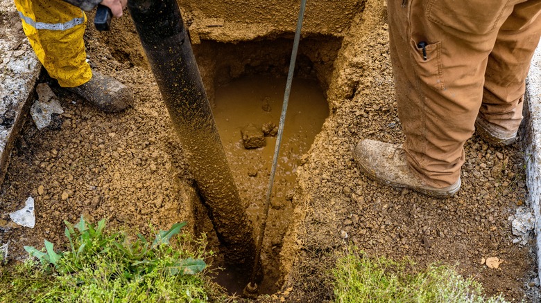Workers repair a busted water main pipe on muddy ground as they wear yellow reflective clothing.