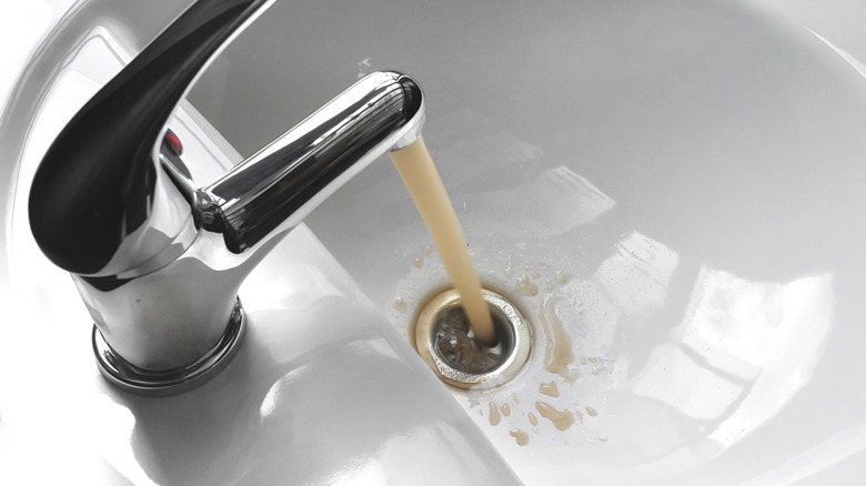 Top view of a stainless steel faucet emitting brown discolored water into a sink