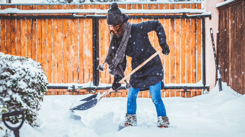 Woman with a hat and scarf shoveling snow into a pile