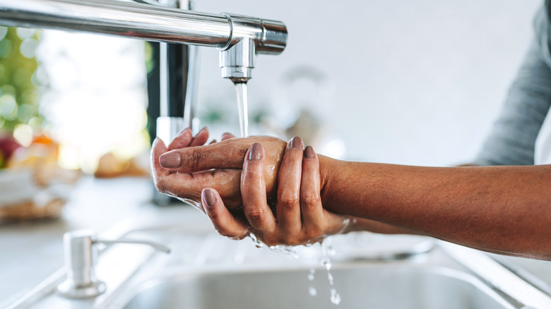 A person washing their hands under a stream of water from a sink faucet