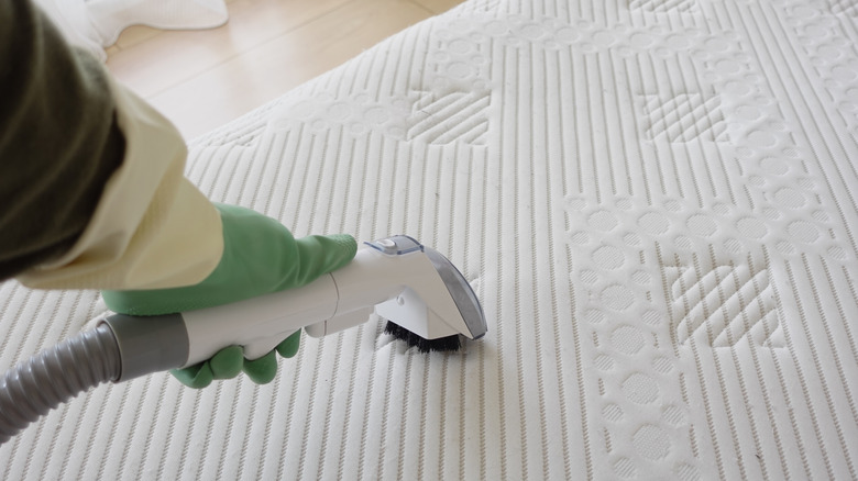 A person cleans a mattress using a steamer