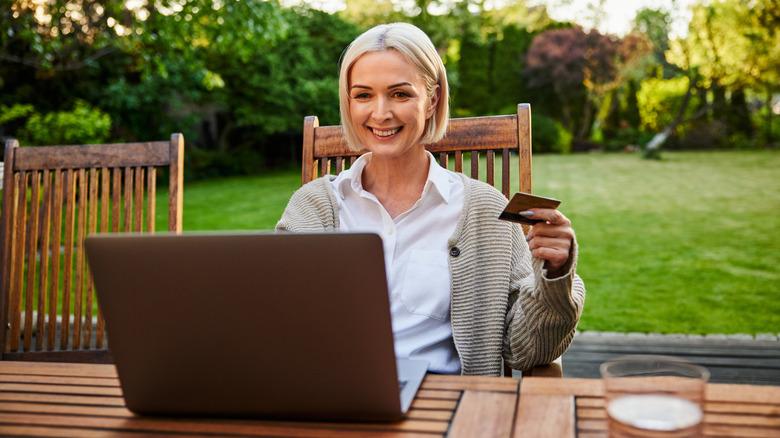 Woman shopping for bird baths on a laptop at a patio table in her backyard