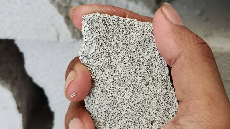 A person holding a chunk of cellular concrete in their hand