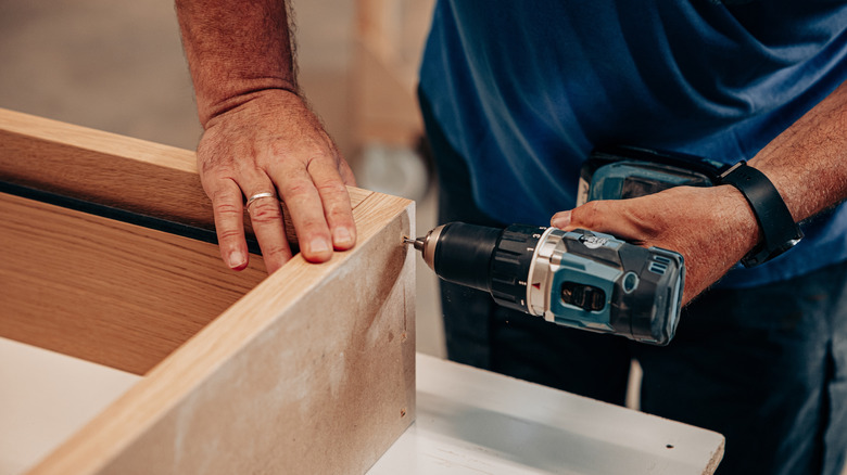 A person using drill on a wood frame