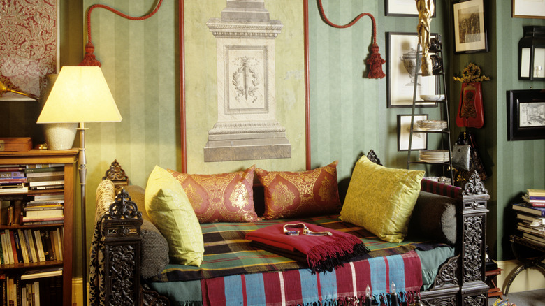 A maximalist lounge area with colorful couch throws and green striped wallpaper