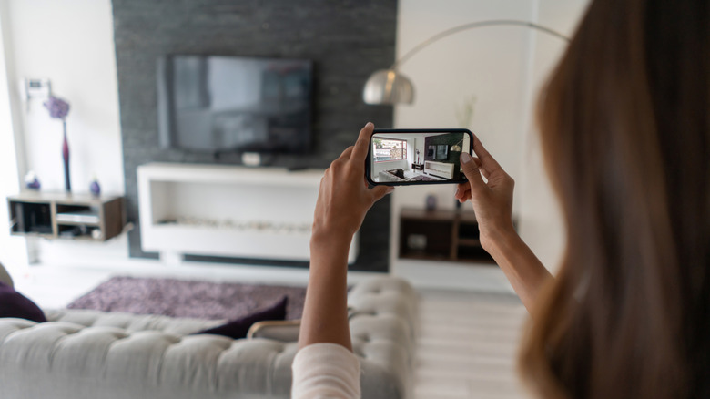 A woman using her phone to take a photo of her living room