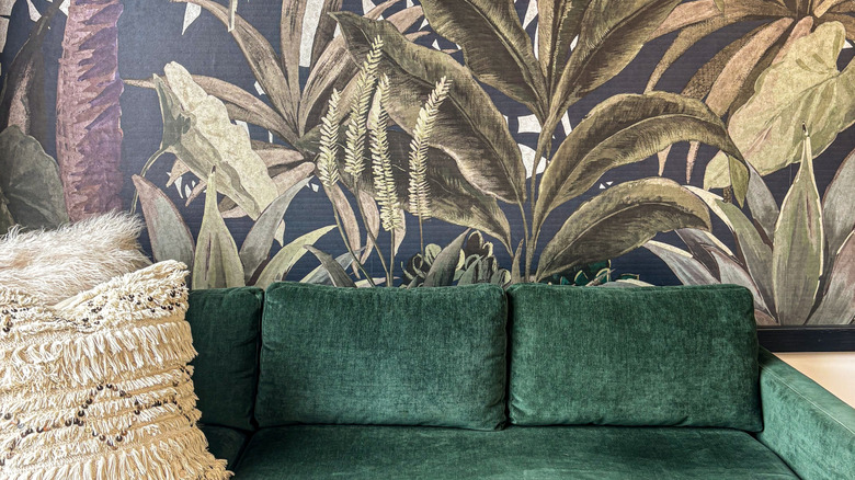 A living room with tropical-themed wallpaper behind a green couch