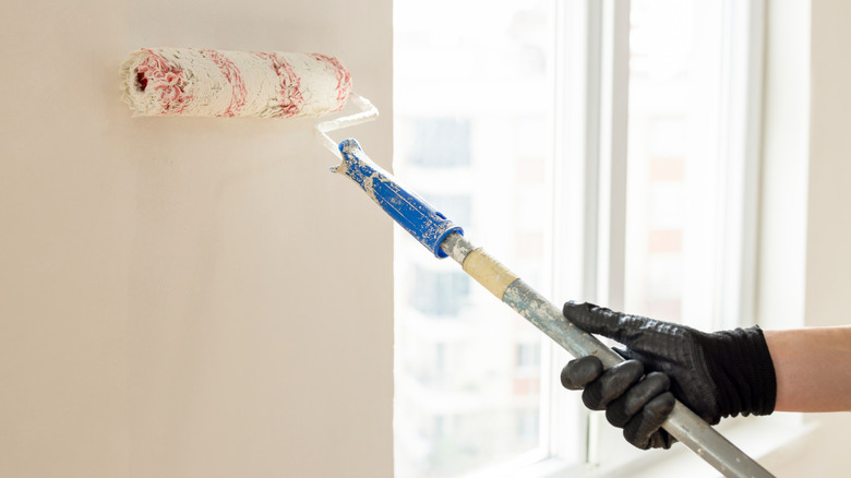 Someone painting with a paint roller on a wall in an apartment