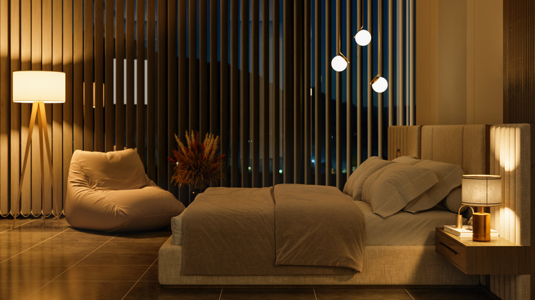 A modern bedroom with dim lighting and a floor to ceiling window at night