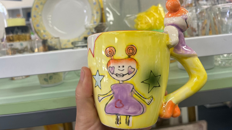 Person holding a whimsical cup in a thrift store