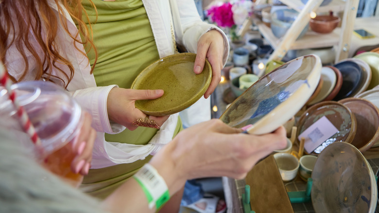 Two women holding decorative dinnerware at a thrift store.