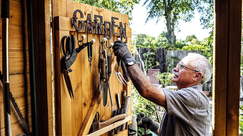 Smiling person hangs up tools on a wooden door on hooks that spell out 