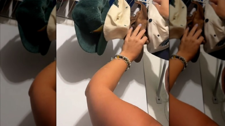 Person hanging baseball caps on bottom of wire shelf with hooks