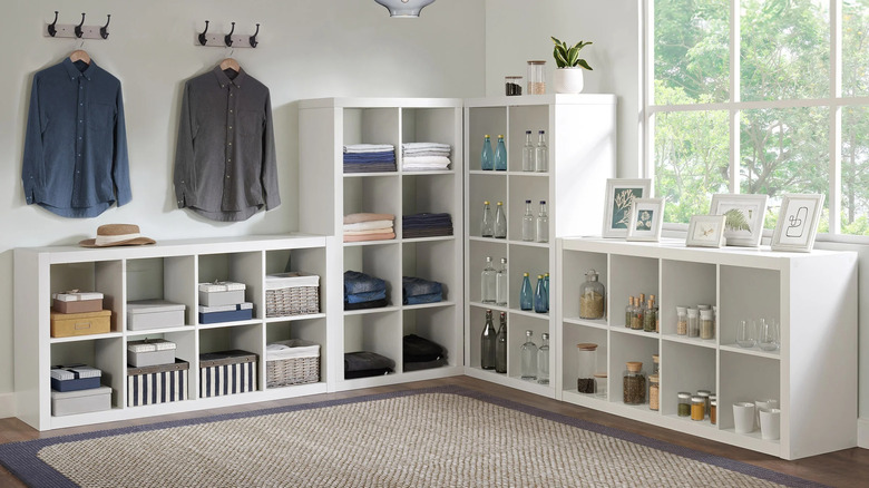 Several room divider shelves with various clothing pieces and other items stacked on them