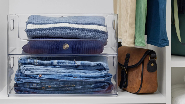 Two Clearly closet storage bins on a closet shelf with jeans and sweaters