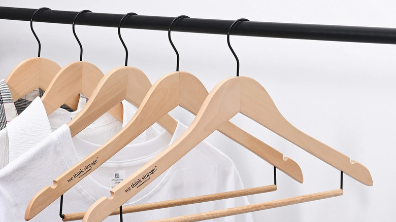 WeThinkStorage wooden hangers hanging on a black closet rod with shirts hanging on some hangers
