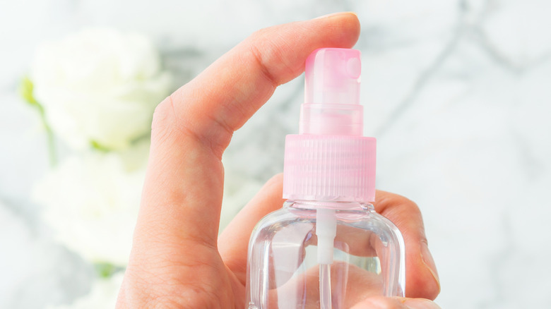 A hand holding a water spritzer with a pink cap