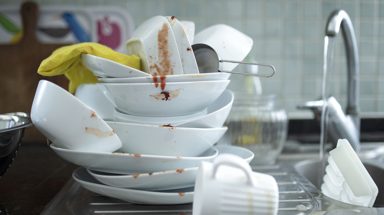 A stack of dirty serving dishes sitting near a sink