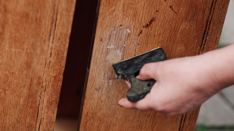 A hand applying wood filler with a spatula