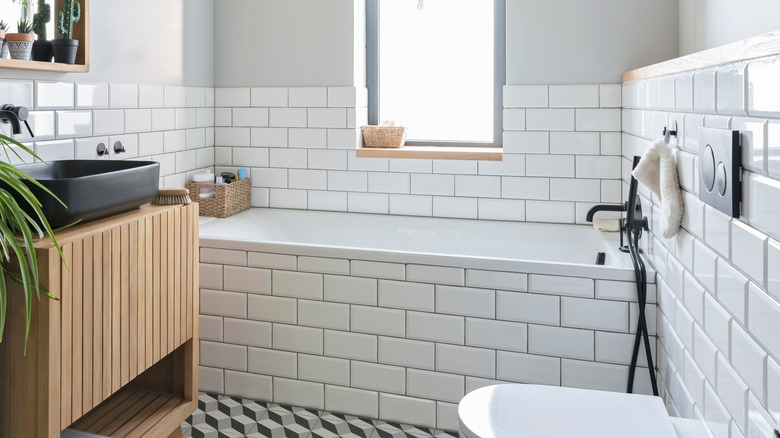 White tiles, wooden cabinet and mirror and bathroom sink in black colour in a bathroom.