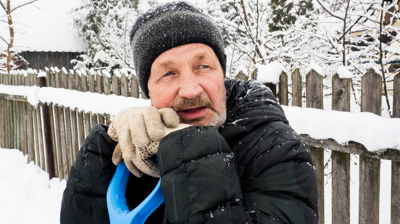 older man shoveling snow rests 