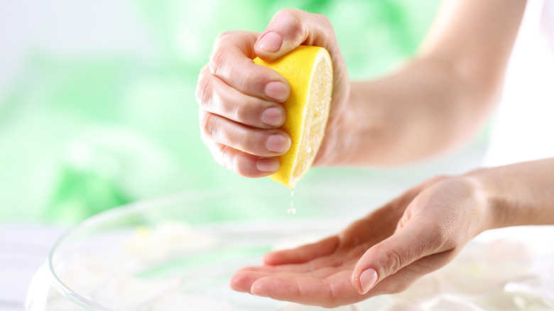 A person squeezing half a lemon over their hands