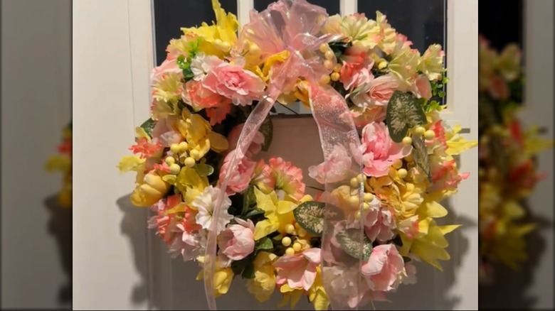A yellow and pink floral wreath with a large bow decorates a front door.