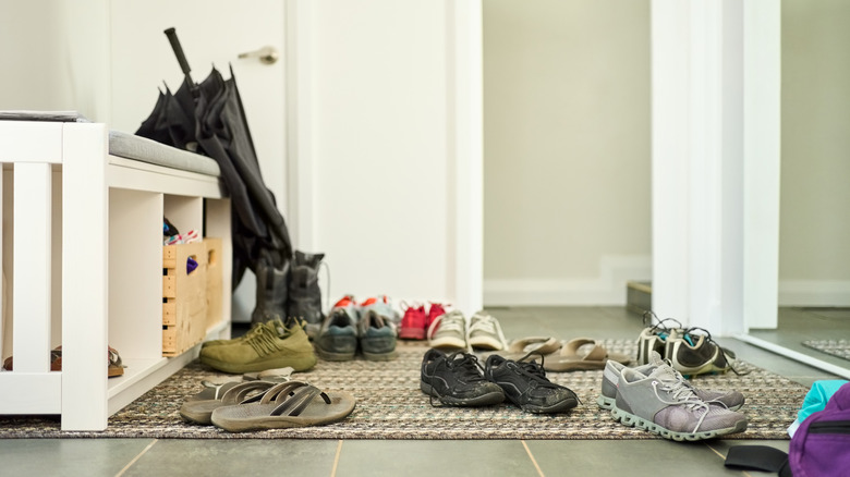 Shoes scattered on the floor of a house on top of a rug near a bench in the entryway