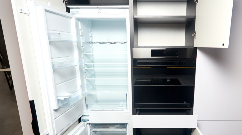 An integrated refrigerator is place among white kitchen cabinetry and a black oven
