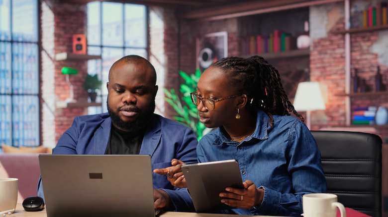 Young couple plans, writes and consults computer and tablet at home.