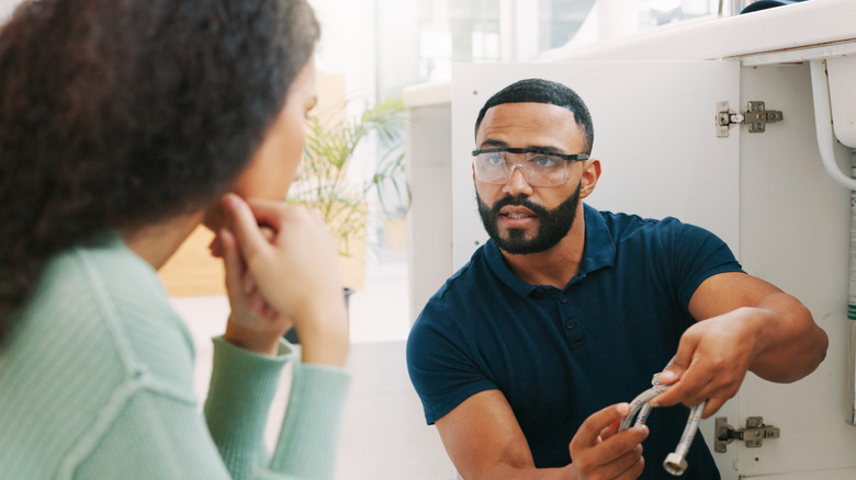 A man in safety goggles shows plumbing to a woman.