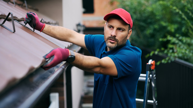 Maintenance worker fixing the tiles on the roof of a house.