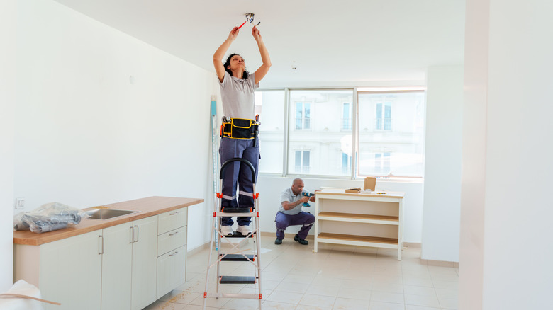 Female electrician standing on ladder to work on ceiling light