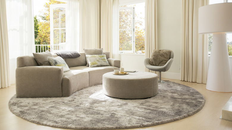 Curved grey sofa, round stool, and side chair on a circular grey rug.