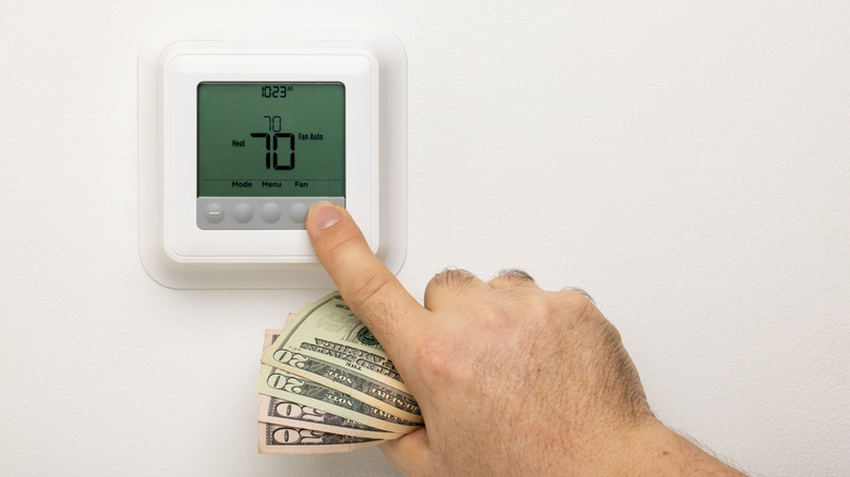 Person setting thermostat while holding money