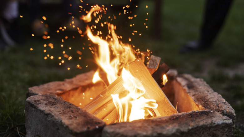 A closeup of a firepit with wood and orange flames and sparks