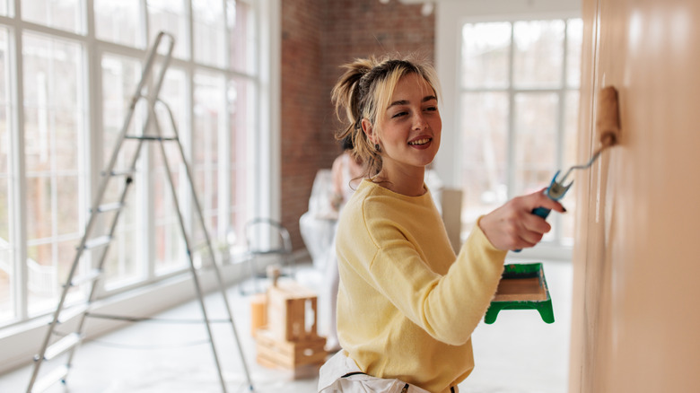 A woman painting her walls with pale clay toned paint