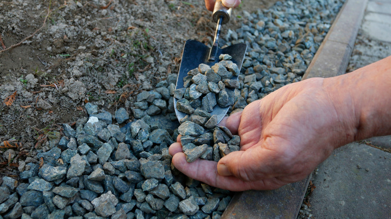 Person laying down gravel along the edge of a driveway