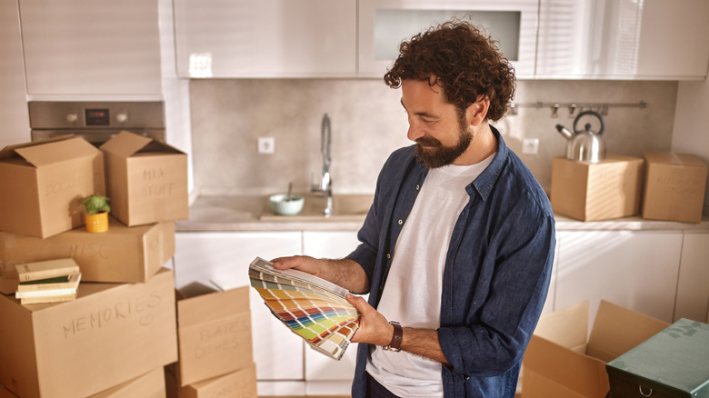 A man stands in a kitchen with moving boxes, holding a paint color fan deck
