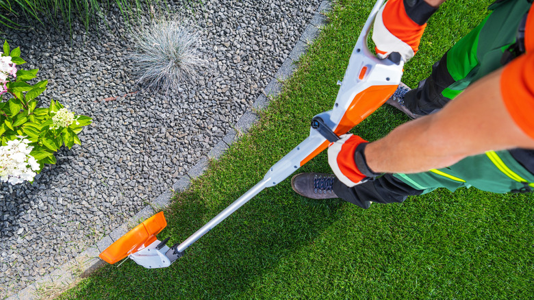 Man using string trimmer to clean up garden edge