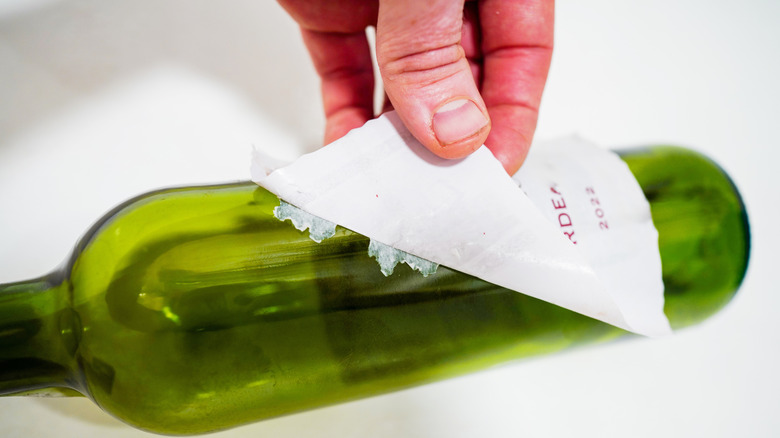 Close up of person trying to peel a sticker off a green glass bottle