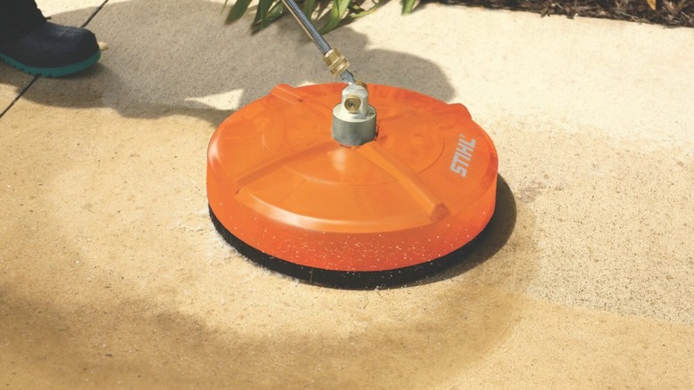 A person cleaning a stone-slab pathway with Stihl's Rotary Surface Cleaner