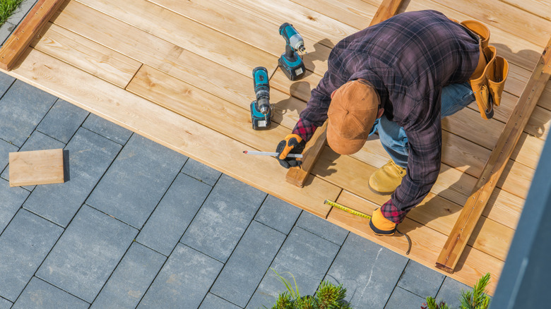 A builder measures the wood while building a deck over pavers.
