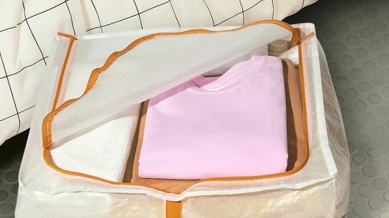 The Pärkla storage case filled with seasonal clothes sitting next to a bed