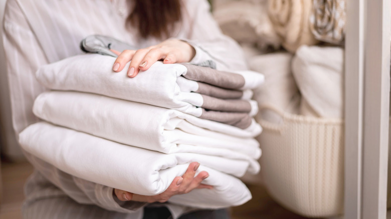 A person with folded linens with a full linen closet in the background