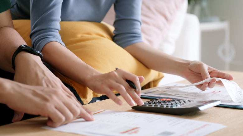 two people calculating prices from receipts and reports on a calculator