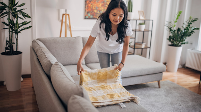 Woman folding a blanket on a gray sofa