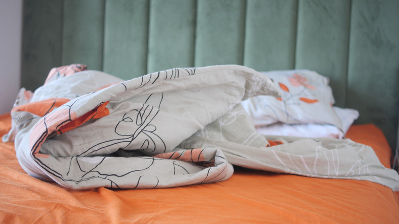 Bed with messy blanket on orange sheet in bedroom setting